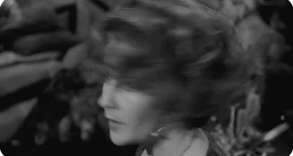 Descrição: Gif animado, no qual aparece a imagem em preto e branco de uma mulher que olha para a câmera, com expressão de surpresa. Ela é loira e tem olhos claros. 